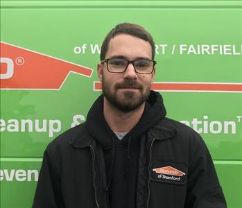Male employee with brown hair and glasses smiling in front of green van.